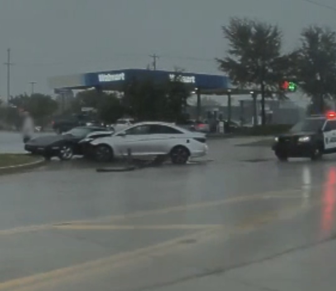 A damaged white sedan against a dark sports car near the Walmart gas station on Tecumseh Road in the rain, with a Norman police car nearby